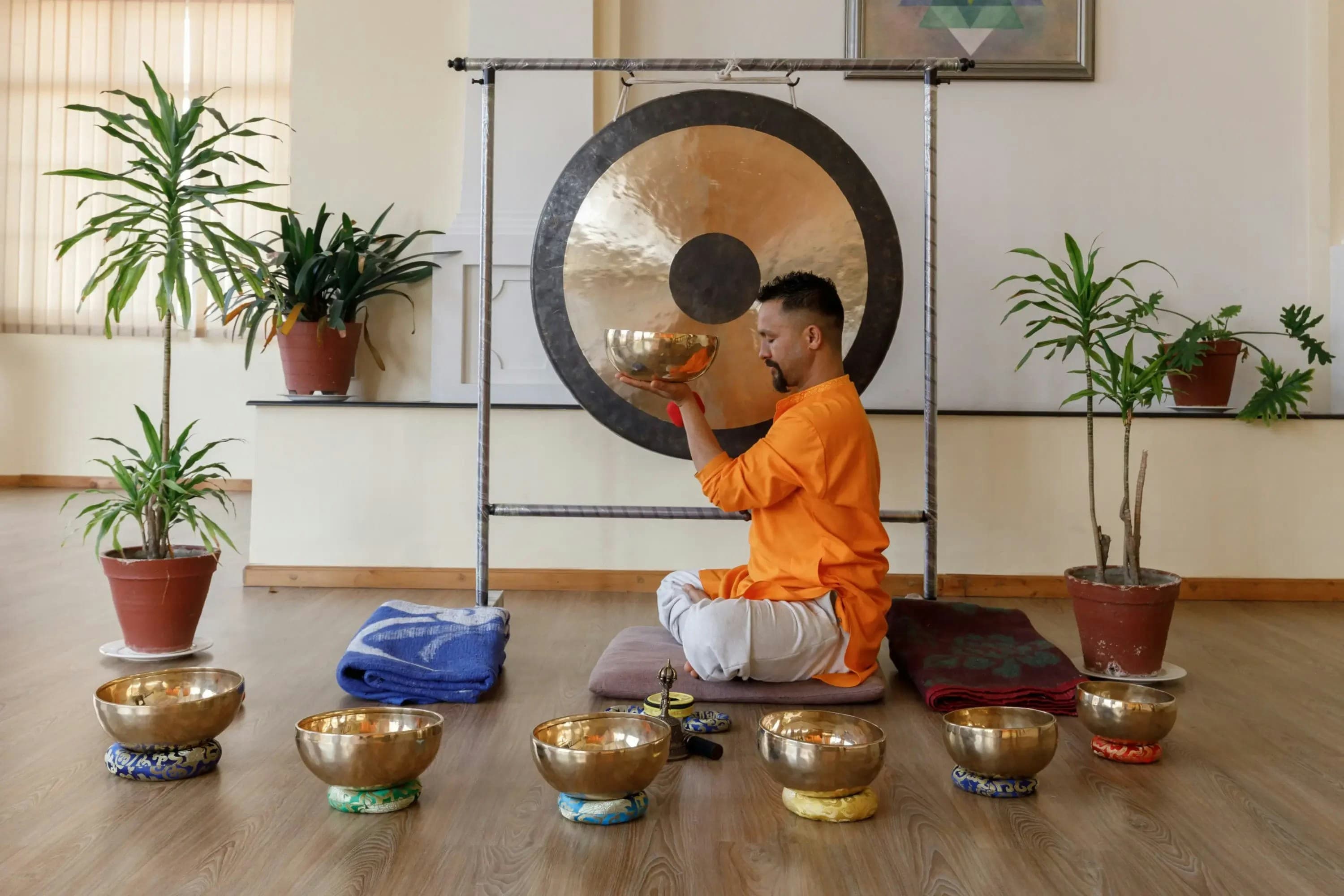 A practitioner playing a gong surrounded by singing bowls in a calm studio